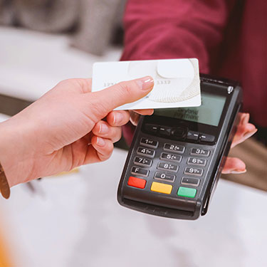 Close up of customer waving credit card over credit card terminal for purchase.